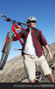Young Man Carrying Mountain Bike in front of hills