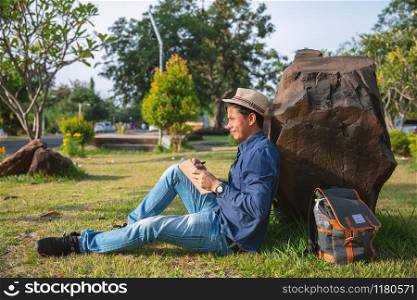 Young man caucasian enjoy writing a diary book with happy face in the garden. Happy relaxing writer taking a note in the park.