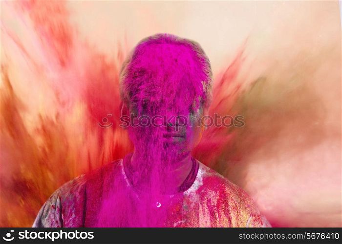 Young man celebrating Holi festival with powder paints over colored background
