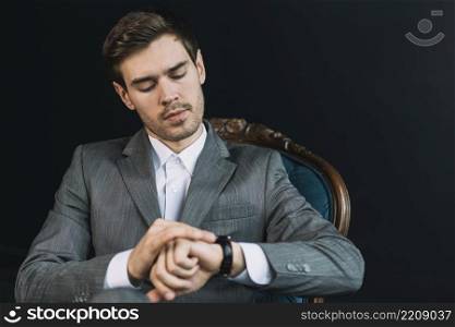 young man checking time his watch against black background