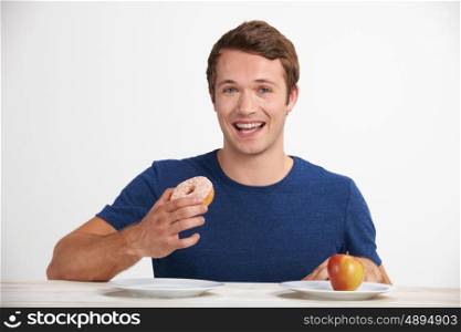 Young Man Choosing Between Doughnut And Cake For Snack