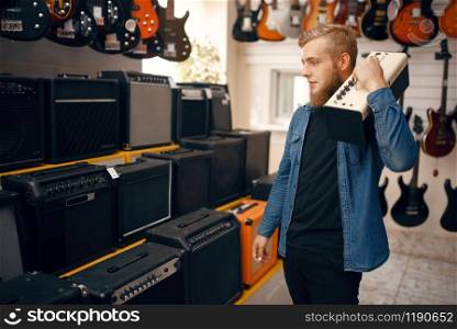 Young man choosing combo amplifier for electric guitar in music store. Assortment in musical instruments shop, male musician buying equipment