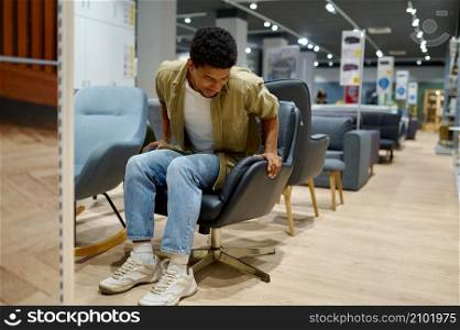 Young man choosing soft comfortable leather chair for office or home in furniture store. Young man choosing chair in furniture store