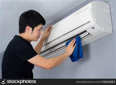 young man cleaning the air conditioner with cloth at home