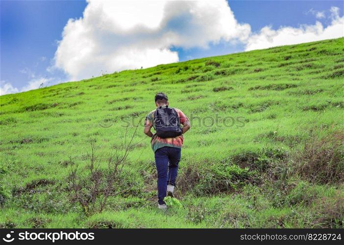 Young man climbing a hill with blue sky , back traveler climbing a hill, back guy hiking