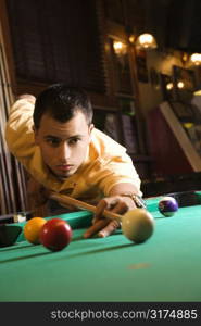 Young man concentrating while aiming at pool ball while playing billiards.