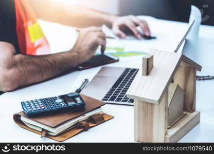 Young man construction worker or engineer working at desk with designer equipment to make interior design at workplace. Real estate business and civil engineering concept.