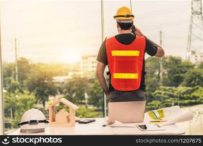 Young man construction worker or engineer working at desk with designer equipment to make interior design at workplace. Real estate business and civil engineering concept.