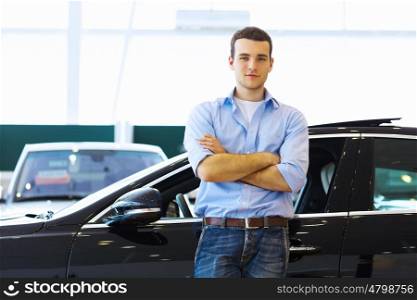 Young man consultant. Handsome young man consultant at car salon standing near car