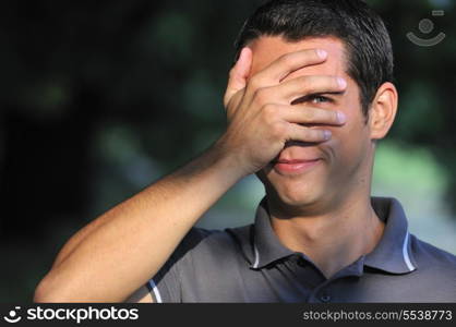 young man cover face with arm and looking on one eye outdoor in nature