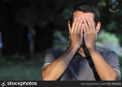 young man cover face with arm and looking on one eye outdoor in nature