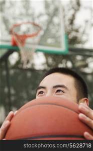 Young man covering his face with basketball