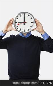 Young man covering his face with clock standing against white background