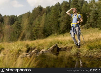 Young man crosses a mountain stream during a hiking on a sunny day