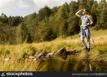 Young man crosses a mountain stream on a sunny day