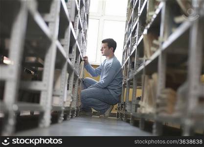 Young man crouches at library shelf