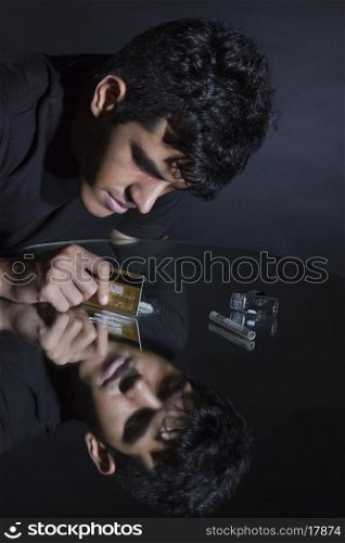Young man cutting cocaine lines with credit card on mirror
