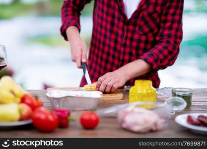 young man cutting vegetables for salad or barbecue grill during outdoor french dinner party near the river on beautiful summer evening in nature