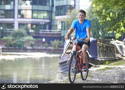 Young Man Cycling Next To River In Urban Setting