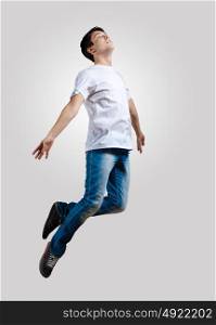 Young man dancing and jumping. Modern slim hip-hop style man jumping dancing on a grey background