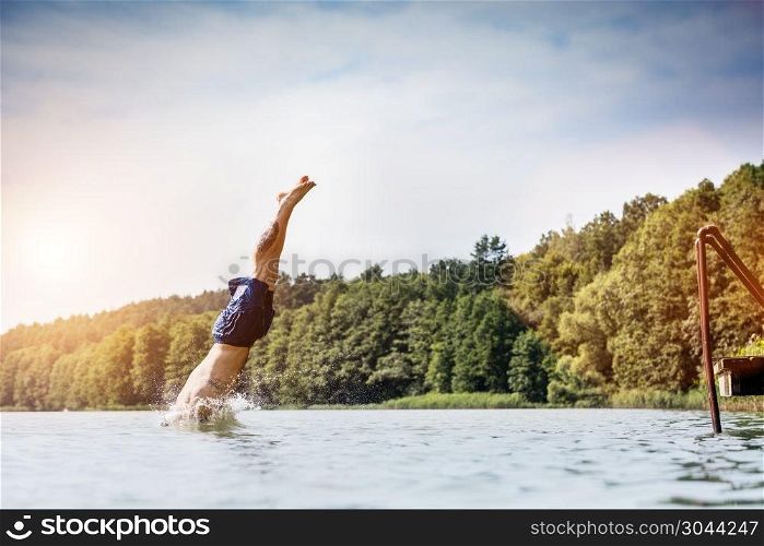Young man diving into a lake. Careless and risky water jump. Summer vacation dangerous outdoor activity. Side view.. Young man diving into a lake.