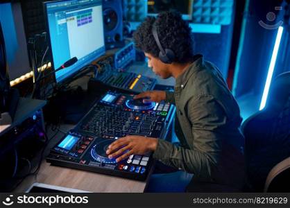 Young man dj broadcasting or recording music on sound mixer in radio station or record studio. Young man paying music on sound mixer in radio station