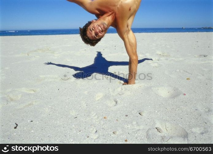 Young man doing a one arm handstand on the beach