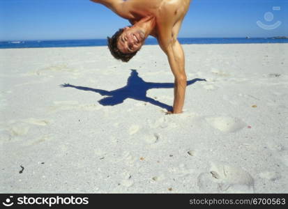 Young man doing a one arm handstand on the beach