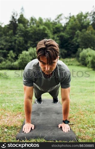 Young man doing push-ups outside on grass during his calisthenics workout. Teenager training outdoors. Young man doing push-ups outside on grass during his calisthenics workout