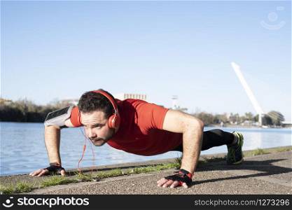 young man doing push-ups with a red t-shirt and music headphones, in an urban environment. healthy living concept