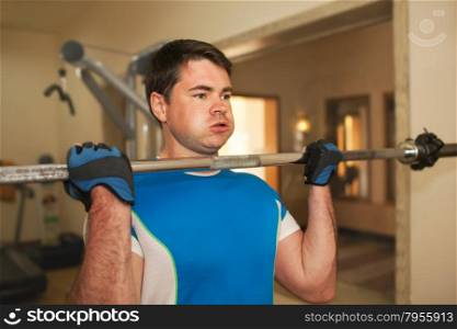 Young man doing strengthen exercise in the gym. He lifting barbell without weight disks