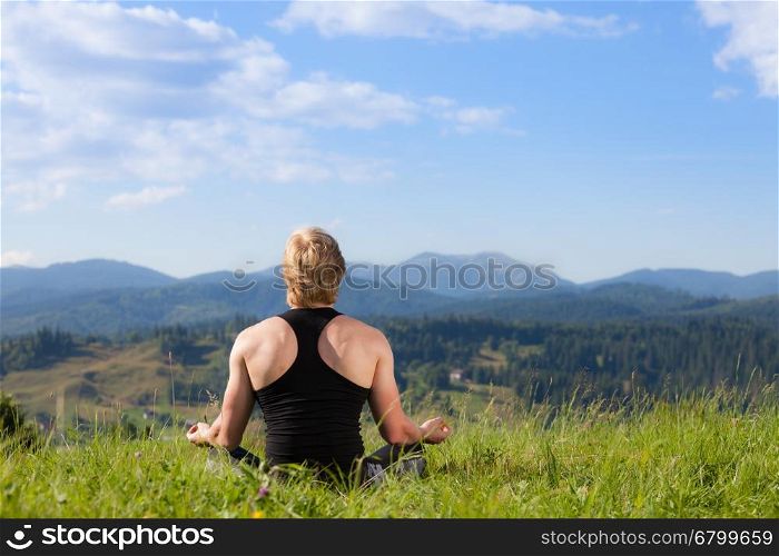 Young man doing yoga exercise at the summer meadow