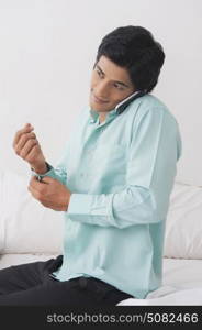 Young man dressing while talking on mobile phone