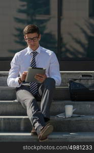Young man drinking coffee outdoors at park and using tablet computer