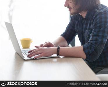 young man drinking coffee while working from home on his laptop computer
