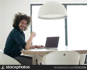 young man drinking coffee while working from home on his laptop computer