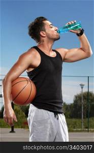 Young man drinking mineral water on a basketball court
