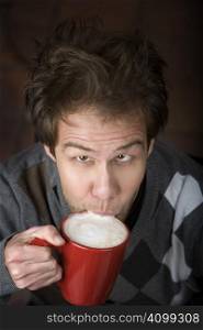 Young man drinking speialty coffee drink from red mug