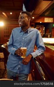 Young man drinks fresh beer at the counter in bar. People relax in pub, night lifestyle, male person with glass of alcohol beverage. Young man drinks fresh beer at the counter in bar