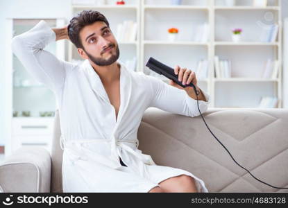 Young man drying hair at home with a hair dryer blower