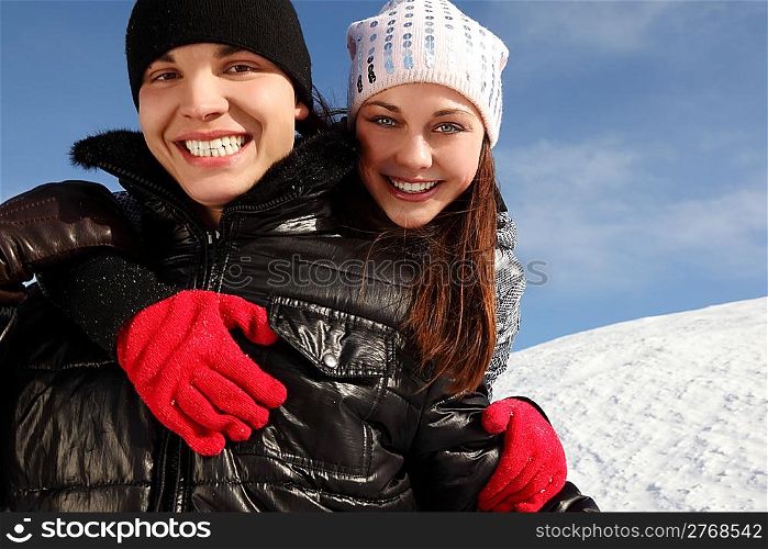 young man embracing girl from back, smiling and looking at camera, winter day