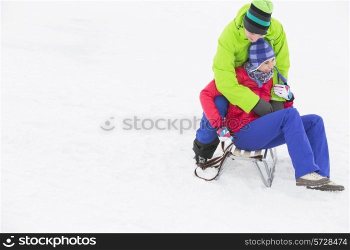 Young man embracing woman on sled in snow