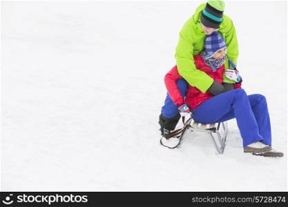 Young man embracing woman on sled in snow