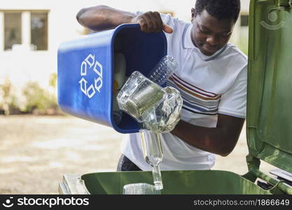 Young Man Emptying Household Recycling Into Green Bin
