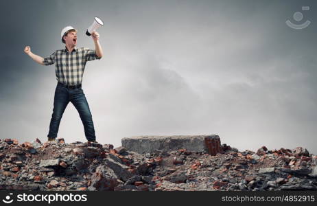 Young man engineer screaming emotionally in megaphone. Builder making announcement