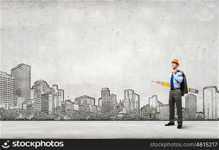 Young man engineer with huge pencil in hands and construction sketches at background. Male architect