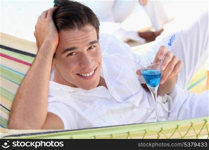 Young man enjoying a cocktail in a hammock