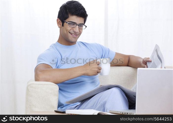 Young man enjoying cup of coffee at home while looking at laptop