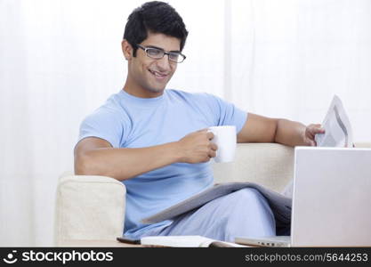 Young man enjoying cup of coffee at home while looking at laptop