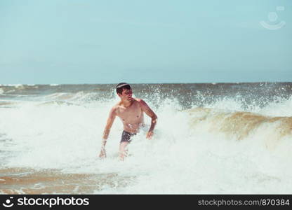 Young man enjoying the high waves in the sea during a summer vacations. Spending a summer holiday by the sea